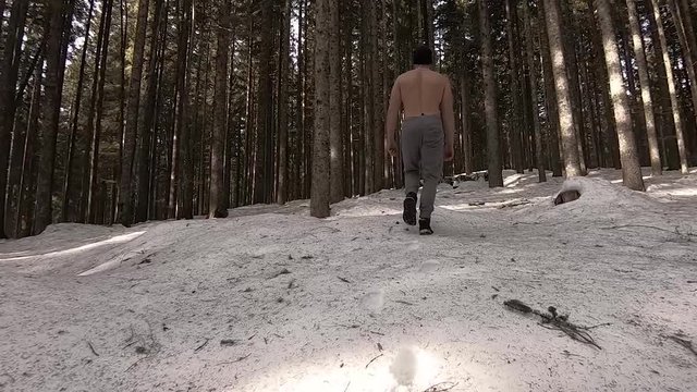 Forward moving following view of ice man without shirt walking on snow