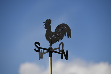 A weathercock in front of a blue sky.