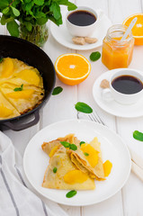 Crepe suzette with orange sauce and a cup of coffee on a white wooden background. Tasty and fragrant breakfast.