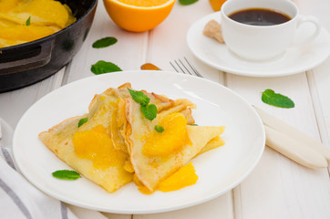 Crepe suzette with orange sauce and a cup of coffee on a white wooden background. Tasty and fragrant breakfast.