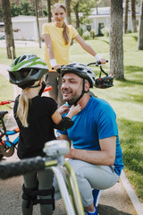 Little girl helping her joyful father to put on bicycle helmet