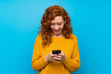 Redhead woman with yellow sweater sending a message with the mobile