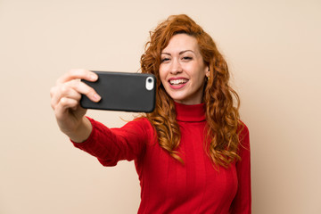 Naklejka premium Redhead woman with turtleneck sweater making selfie with cellphone