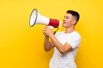 Young handsome man over isolated yellow background shouting through a megaphone