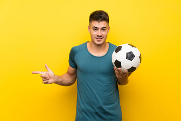 Handsome young football player man over isolated yellow background surprised and pointing finger to the side