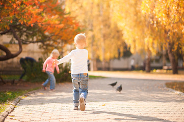 Obraz premium Happy children play in the park closeup. Boy and girl run and have fun in the autumn in the sun and copy space. Happy childhood moments.