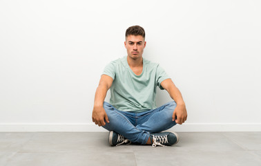 Young handsome man sitting on the floor sad