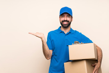 Delivery man with beard over isolated background holding copyspace imaginary on the palm to insert...