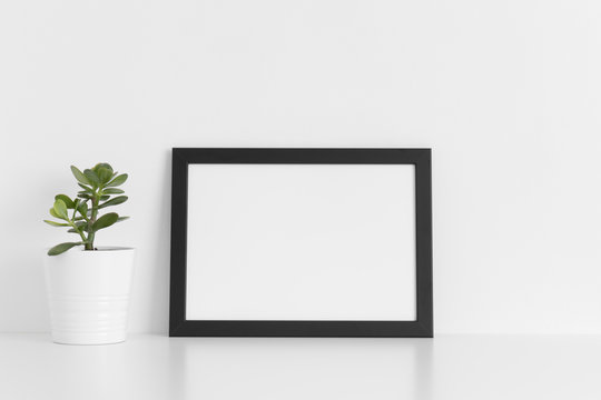 Black frame mockup with a crassula plant in a pot on a white table.Landscape orientation.