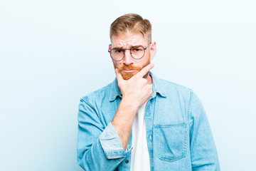 young red head man looking serious, thoughtful and distrustful, with one arm crossed and hand on...