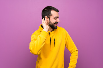Fototapeta premium Handsome man with yellow sweatshirt listening to something by putting hand on the ear