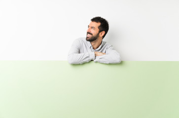 Young handsome man with beard holding a big green empty placard happy and smiling