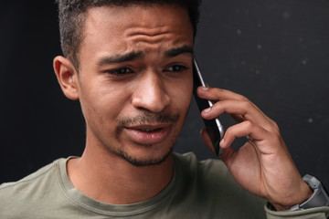 Image of confused african american guy talking on cellphone