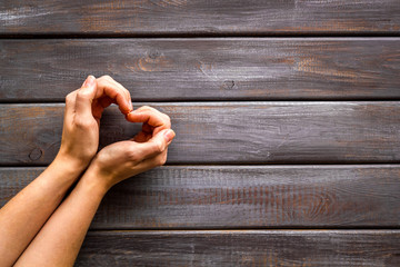Heart icon. Hands forming a heart on dark wooden background top view copy space
