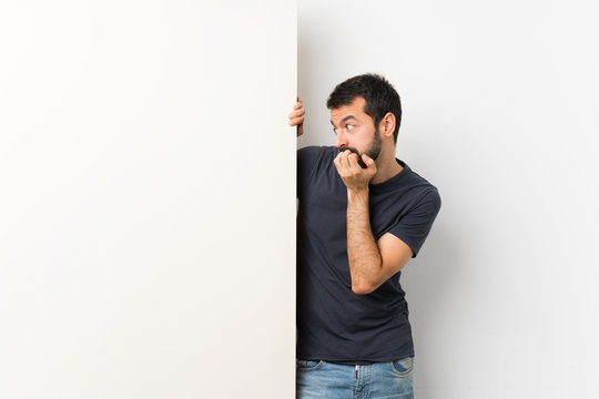 Young handsome man with beard holding a big empty placard nervous and scared putting hands to mouth