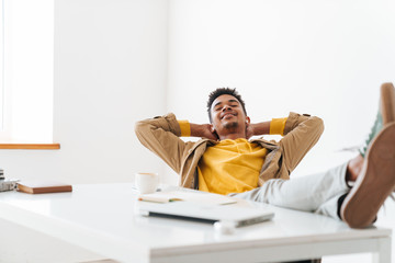 Image of african american guy smiling and sitting on chair in office
