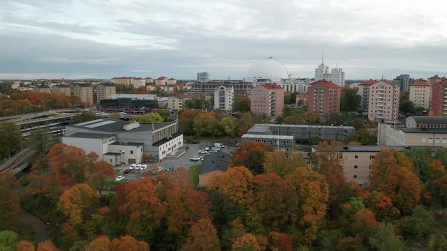 Aerial view of Stockholm Ericsson Globe. Drone flies forwards over buildings and urban park.