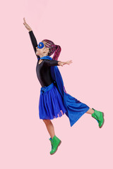 Vertical view. Little girl plays superhero. Kid on the background of bright pink wall, wear in colorful clothes green boots, pink hair. Girl power concept.
