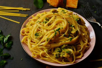 Spashetti on a dark background. Pasta in a pink beautiful plate. Pasta with broccoli and cream, delicious noodles with cheese.
