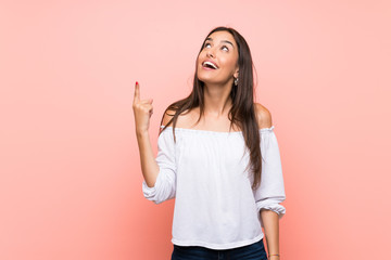 Young woman over isolated pink background pointing up and surprised