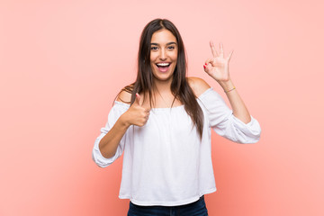 Young woman over isolated pink background showing ok sign and thumb up gesture