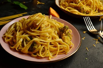 Spashetti on a dark background. Pasta in a pink beautiful plate. Pasta with broccoli and cream, delicious noodles with cheese.
