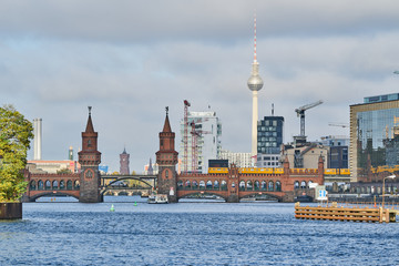 Obraz premium Die Berliner Oberbaumbrücke überspannt die Spree im Morgenlicht mit dem Rathaus, dem Fernsehturm und mehreren Baukränen im Hintergrund