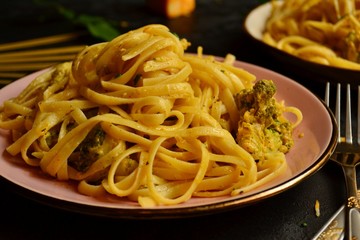 Spashetti on a dark background. Pasta in a pink beautiful plate. Pasta with broccoli and cream, delicious noodles with cheese.