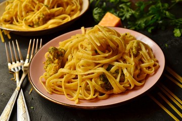 Spashetti on a dark background. Pasta in a pink beautiful plate. Pasta with broccoli and cream, delicious noodles with cheese.