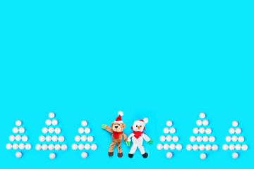 Cute New Year's toys on a blue background. Snowman and bear in Santa Claus hats and Christmas trees made of Christmas balls.  Copy space. New Year card.
