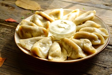 Dumplings in a beautiful plate. Dumplings on a wooden background. Wooden table background with autumn leaves. Appetizing little pie with filling. Traditional homemade food.