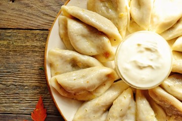 Dumplings in a beautiful plate. Dumplings on a wooden background. Wooden table background with autumn leaves. Appetizing little pie with filling. Traditional homemade food.
