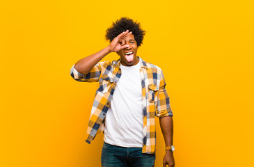 young black man smiling happily with funny face, joking and looking through peephole, spying on...