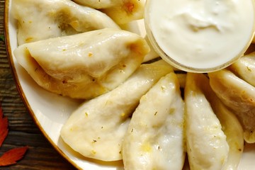 Dumplings in a beautiful plate. Dumplings on a wooden background. Wooden table background with autumn leaves. Appetizing little pie with filling. Traditional homemade food.