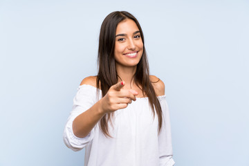 Young woman over isolated blue background points finger at you