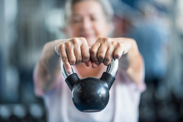 close up of senior holding a weight with his hands in front of the camera at the gym - adult woman working his body to be healthy