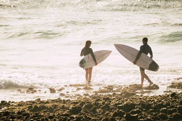 Fototapeta na wymiar couple of two teenagers or adult entering at the water together to go surfing and training - woman and man at the beach touching the water and going surf