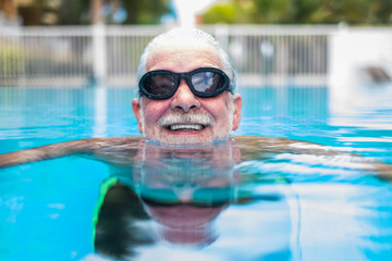 portrait of mature man smiling and looking at the camera in the pool having fun alone - training...