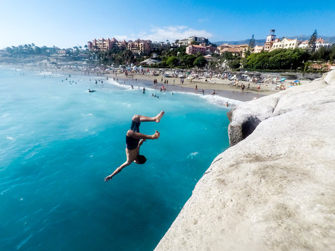 teenager jumping off on the sea by the rocks with some people looking at him - very dangerous activity and guy doing backflip and more freestyle