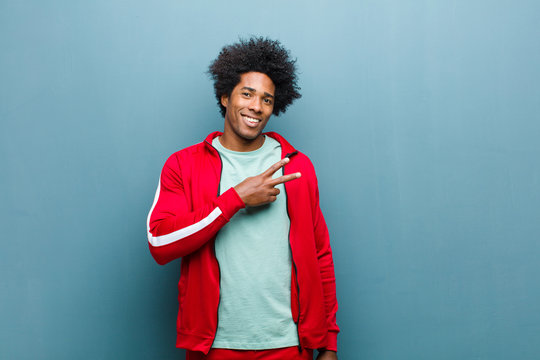 Young Black Sports Man Feeling Happy, Positive And Successful, With Hand Making V Shape Over Chest, Showing Victory Or Peace Against Grunge Wall