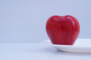 Red apple on a plate on white background.