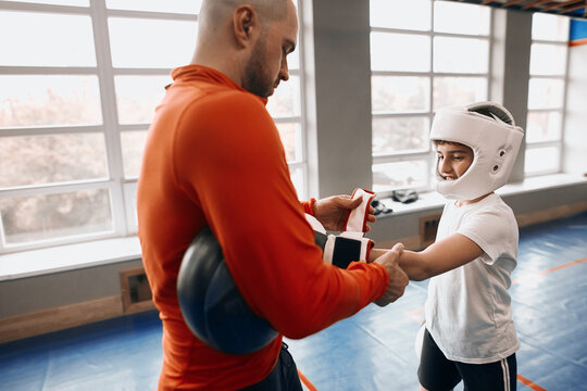 young man helping a boy to put on boxing gloves. close up side view photo. man preparing a kid for boxing