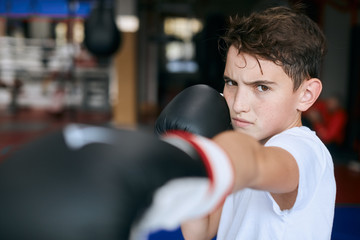 agressive angry boy punching with boxing gloves.close up cropped photo. blurred foreground.