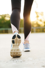 Cropped image of woman wearing tracksuit and sneakers running outdoors