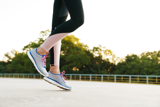 Cropped image of woman wearing tracksuit and sneakers running outdoors
