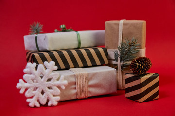 Five gifts are stacked on table, made independently of craft and wrapping paper, decorated with cone, snowflake ribbons and pine branches. A holiday comes to us. Merry Christmas, Happy New Year.