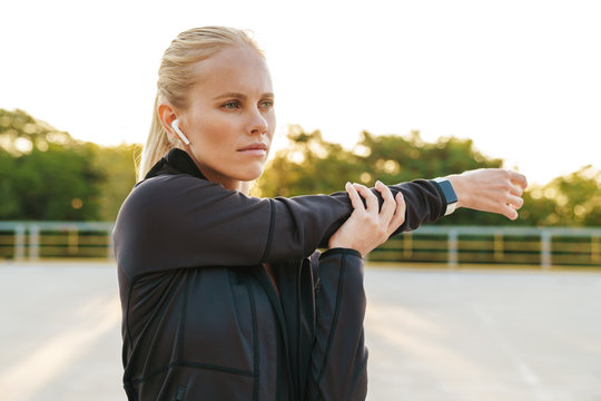 Image of sportswoman wearing tracksuit and earpods doing workout outdoors