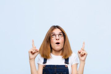 young pretty woman feeling awed and open mouthed pointing upwards with a shocked and surprised look...