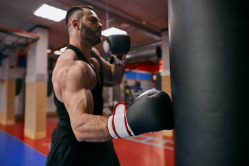 Fototapeta na wymiar Young strong ambitious athlete working out by throwing punches at a heavy punching bag, close up photo. lifestyle, free time, spare time