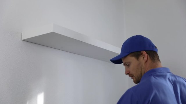 handyman installing shelf on the white wall at home